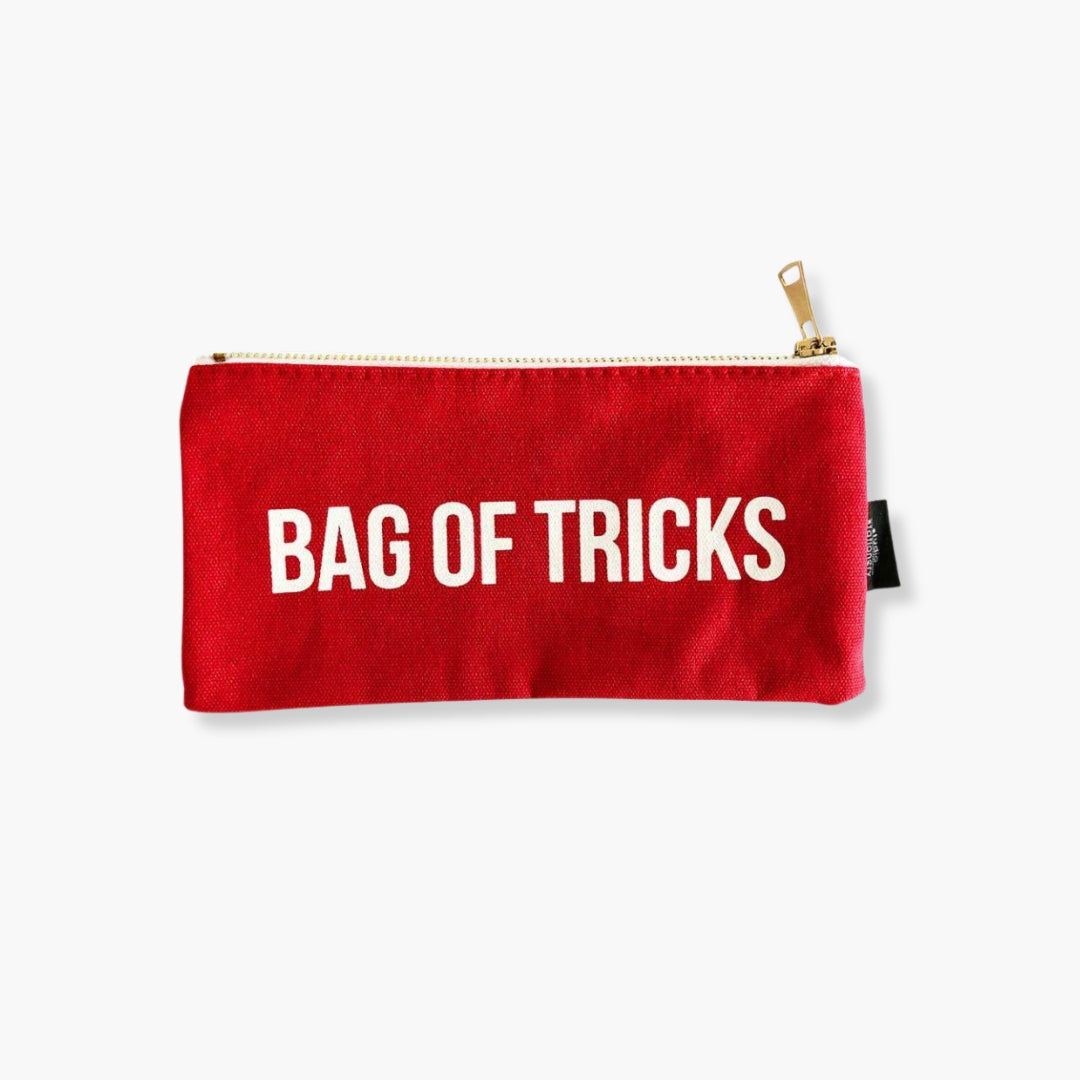 Estuche Canvas Bag of Tricks rojo con texto blanco y cierre dorado.