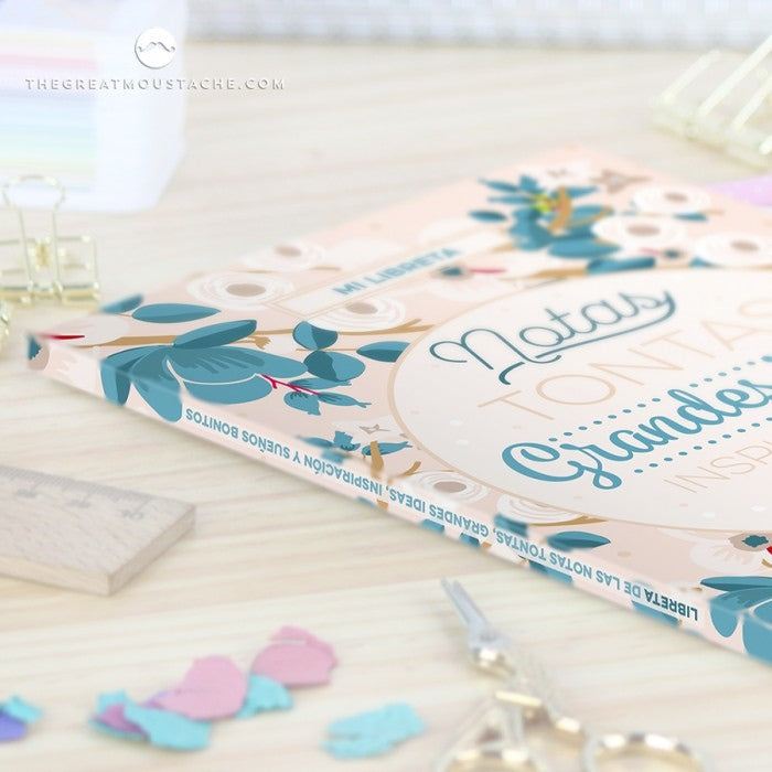 Libreta "Notas Tontas, Grandes Ideas, Inspiración y Sueños Bonitos" con diseño colorido y tamaño A5 sobre mesa de oficina.