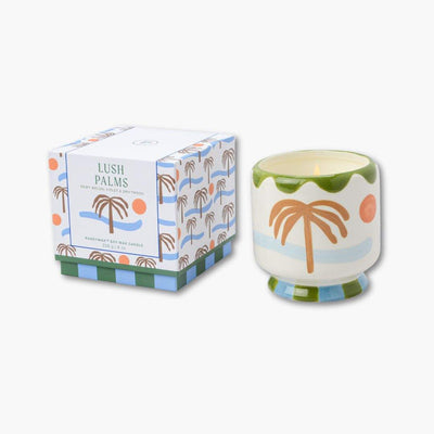 vela perfumada en recipiente de cerámica pintada junto con su caja de cartón de paddywax con dibujo de palmeras
