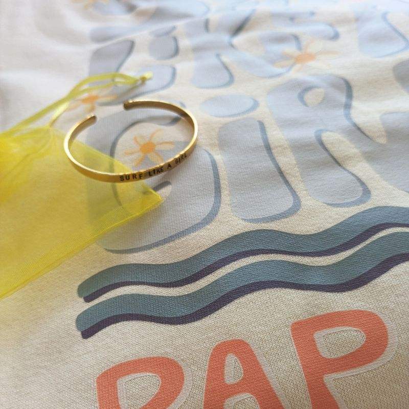 Pack Regalo Sudadera y Brazalete "Surf Like a Girl" Papalum, sudadera ivory con ilustración surfista y brazalete de latón grabado a mano, moda y mensaje para mujeres aventureras.