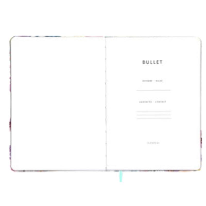 Cuaderno Bullet Journal Mari con páginas punteadas, tapa dura dorada, y cinta de registro.