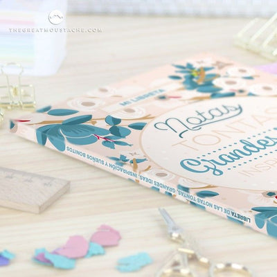 Libreta "Notas Tontas, Grandes Ideas, Inspiración y Sueños Bonitos" con diseño colorido y tamaño A5 sobre mesa de oficina.